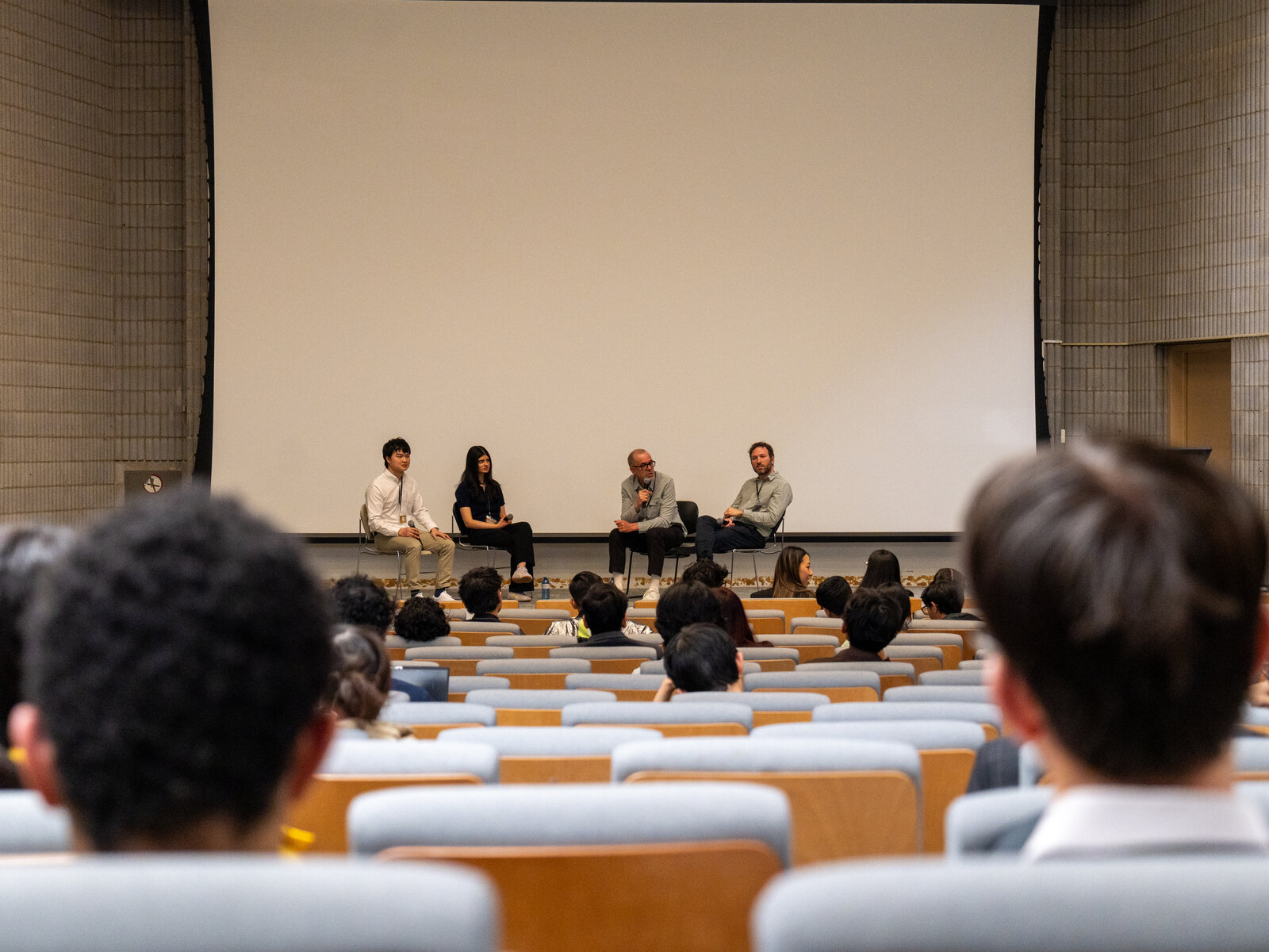 Four panelists on stage with the audience in the foreground, in a lecture hall.