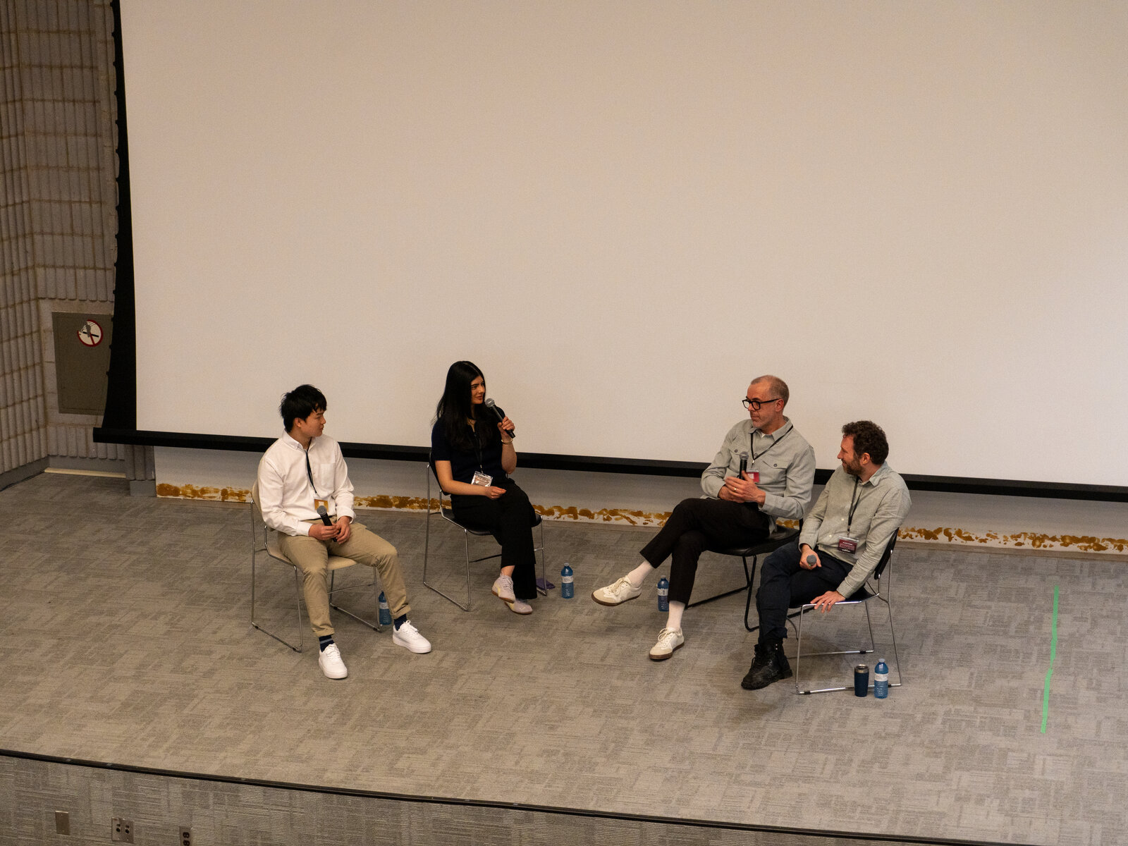 Four panelists seated on stage with microphones and a No Smoking sign visible.