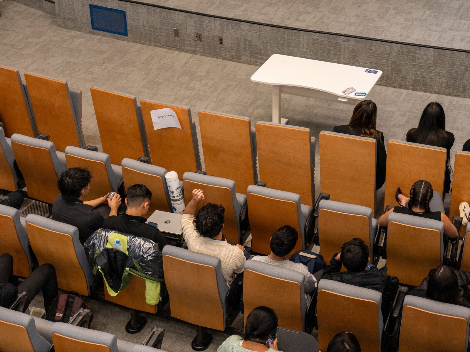 Audience members seated in rows, some with laptops, facing the front of the room.